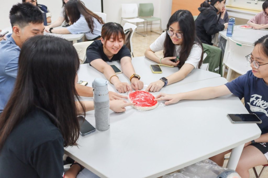 Students point together at the red Xin Ding Ban in the center of the table.