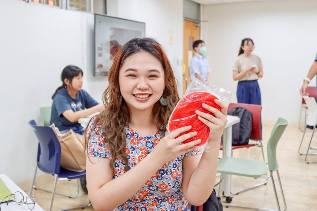 A student smiles while holding up Xin Ding Ban with both hands.